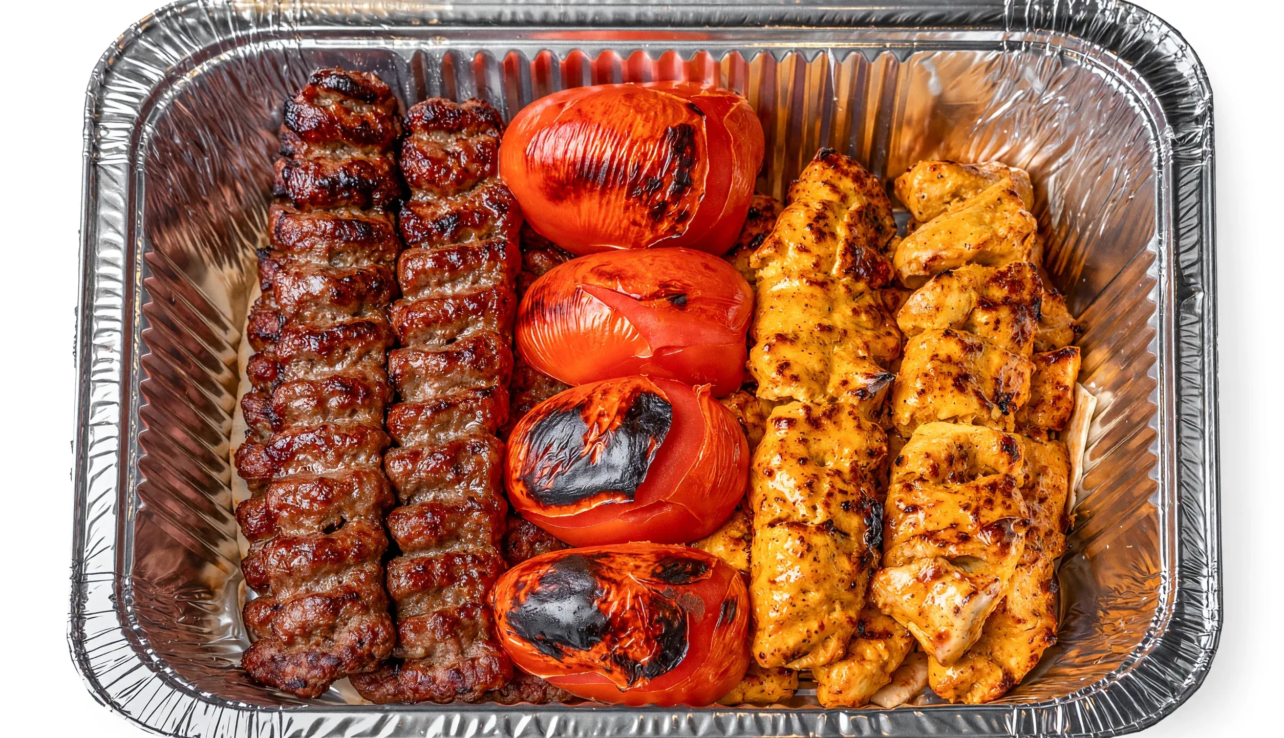 Mixed kabab family platter: beef koobideh skewers, saffron chicken kababs and grilled tomatoes in a large foil tray at AFRA Grill, Saskatoon