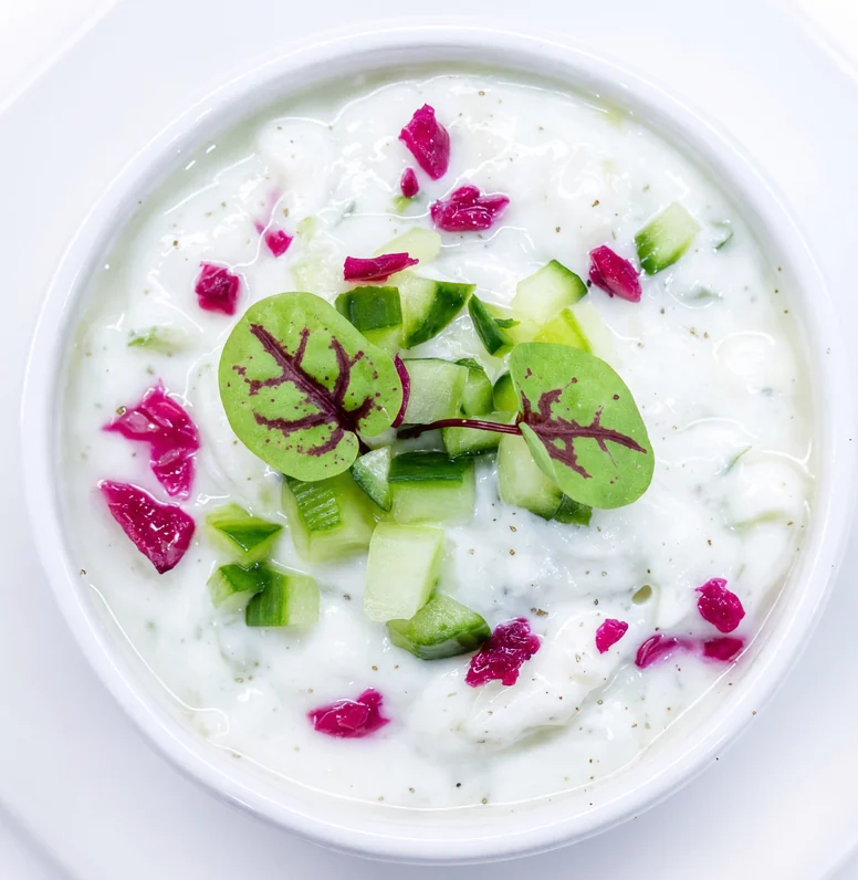 Maust khiar cucumber yogurt dip with diced cucumber, rose petals and microgreens in a white bowl at AFRA Grill, Saskatoon
