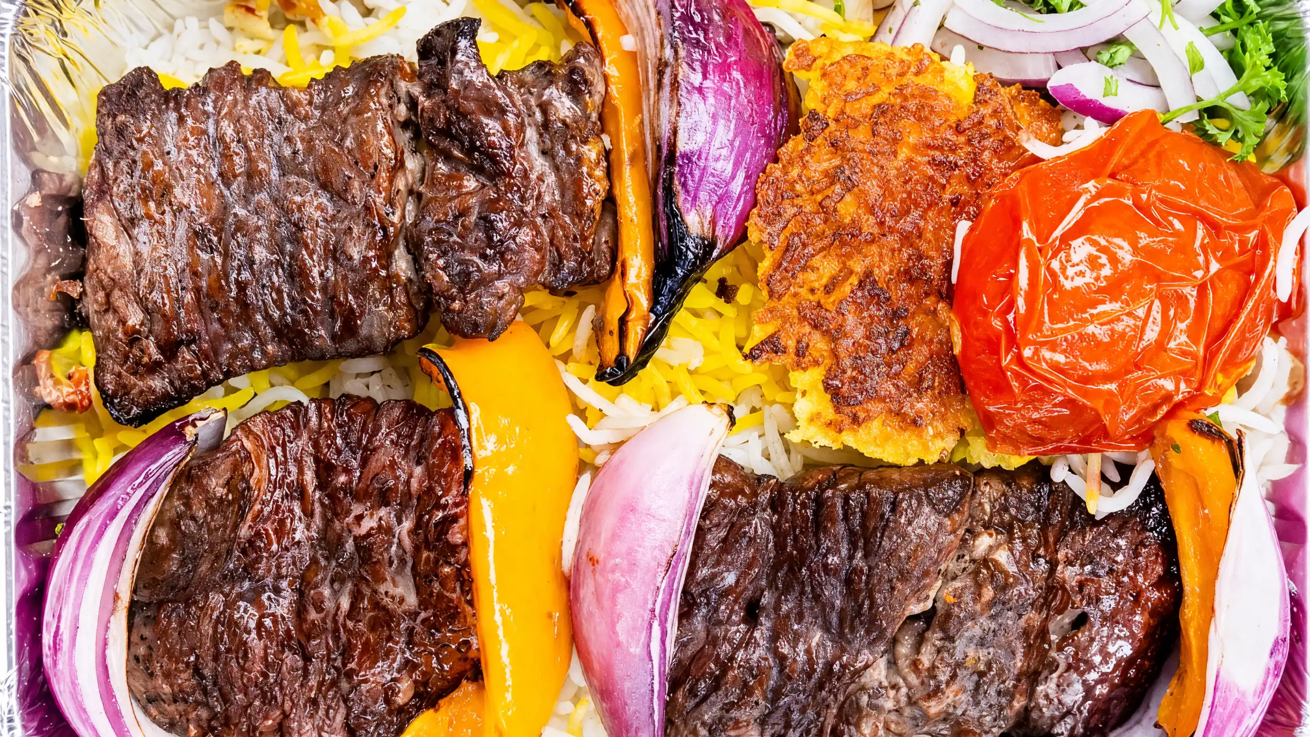 Chenjeh: grilled marinated steak kabab with charred peppers, red onion, a grilled tomato and saffron rice in a foil tray at AFRA Grill, Saskatoon