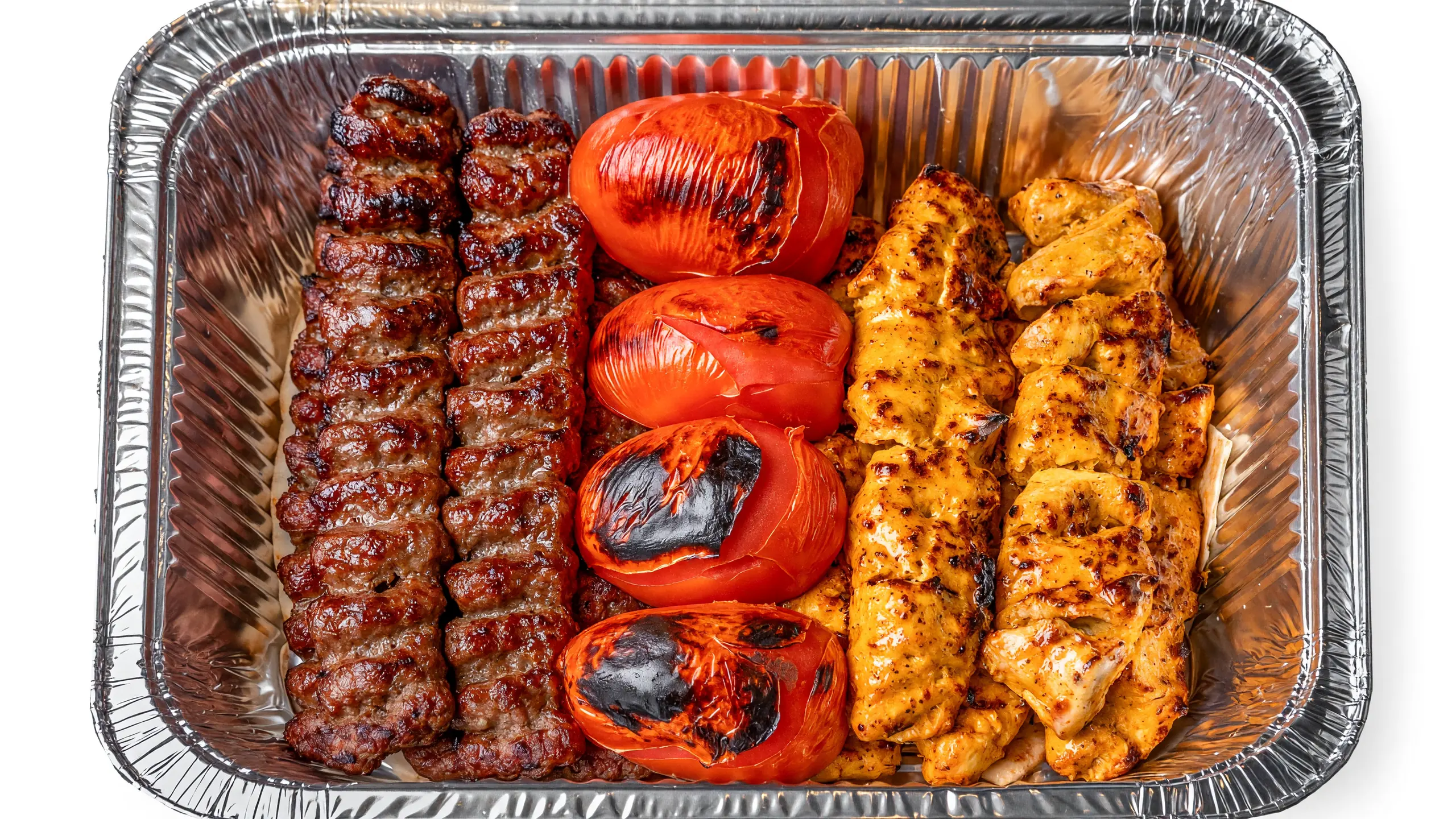 Mixed kabab family platter: beef koobideh skewers, saffron chicken kababs and grilled tomatoes in a large foil tray at AFRA Grill, Saskatoon