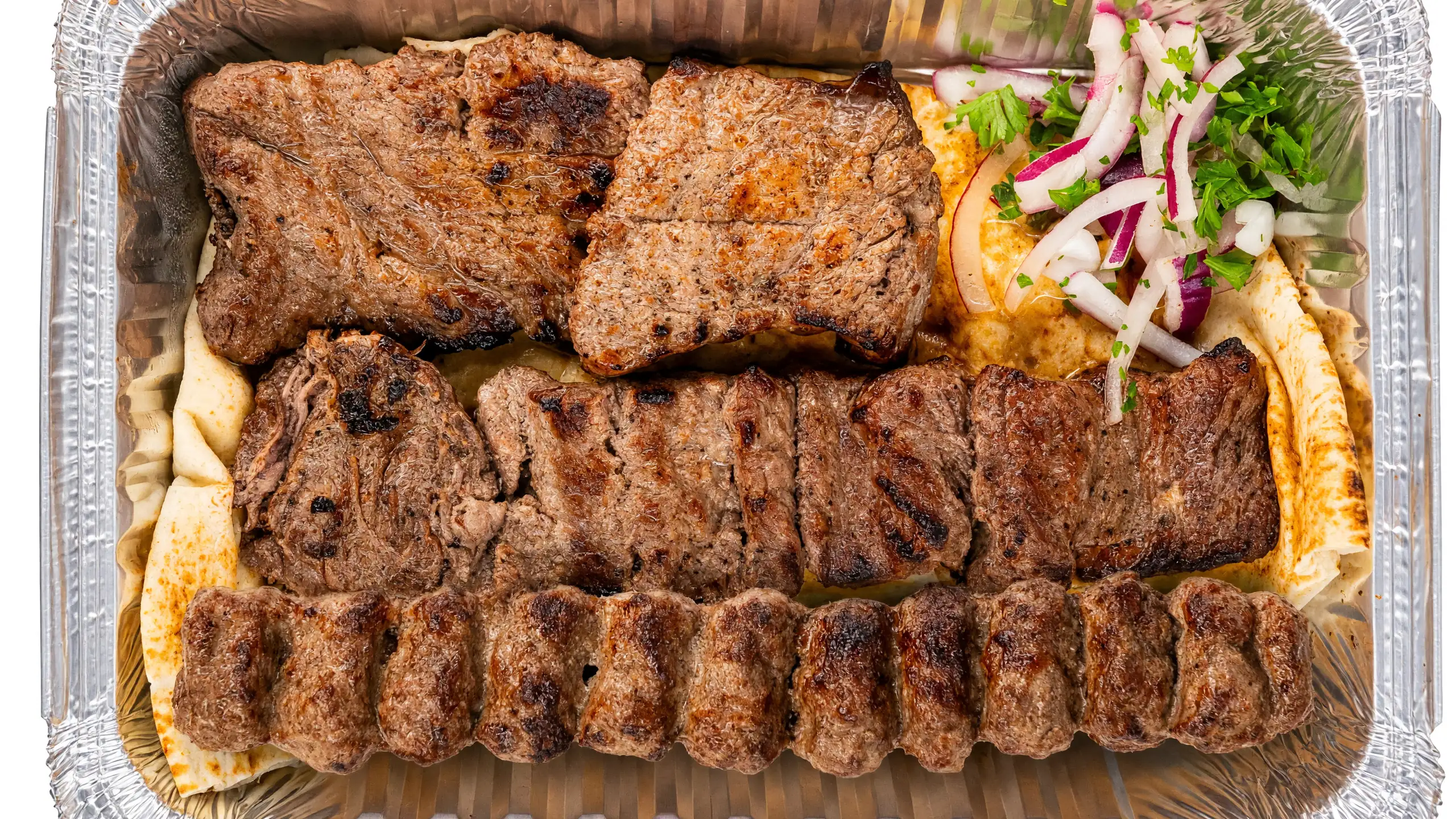 Shazdeh kabab: grilled steak pieces and a beef koobideh skewer on flatbread with sliced onion and herbs in a foil tray at AFRA Grill, Saskatoon
