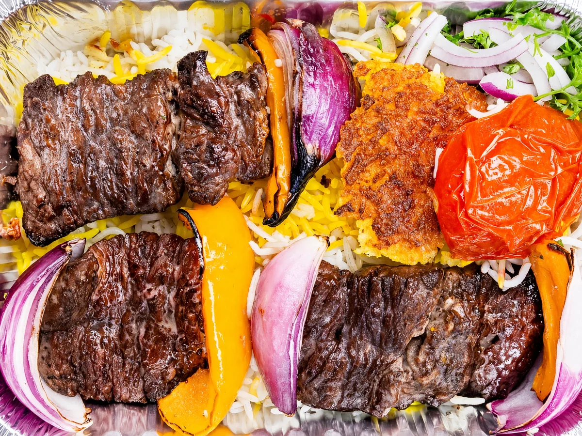 Chenjeh: grilled marinated steak kabab with charred peppers, red onion, a grilled tomato and saffron rice in a foil tray at AFRA Grill, Saskatoon